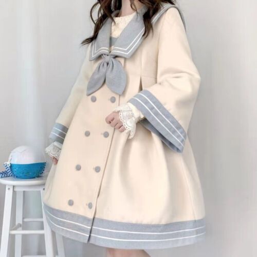 a young woman is wearing a beige wool coat with a sailor collar, a large bow, and blue and white striped trim. the coat has a doublebreasted button closure and a flared skirt. the woman is standing indoors in a welllit room. she is wearing a white lace top underneath the coat.  the overall style of the outfit is reminiscent of japanese lolita fashion.