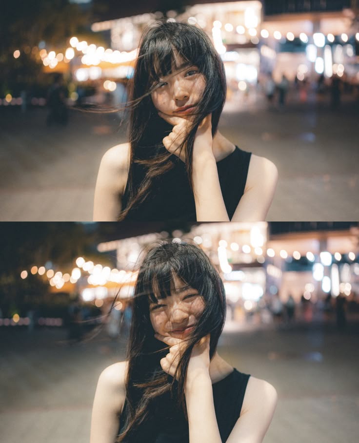 the image shows a portrait of a young woman at night. she has long, dark hair with bangs, and is wearing a black tank top. she is smiling slightly and resting her hand on her chin. the background is blurred, with lights suggesting a street scene. the overall mood is soft and somewhat dreamy.