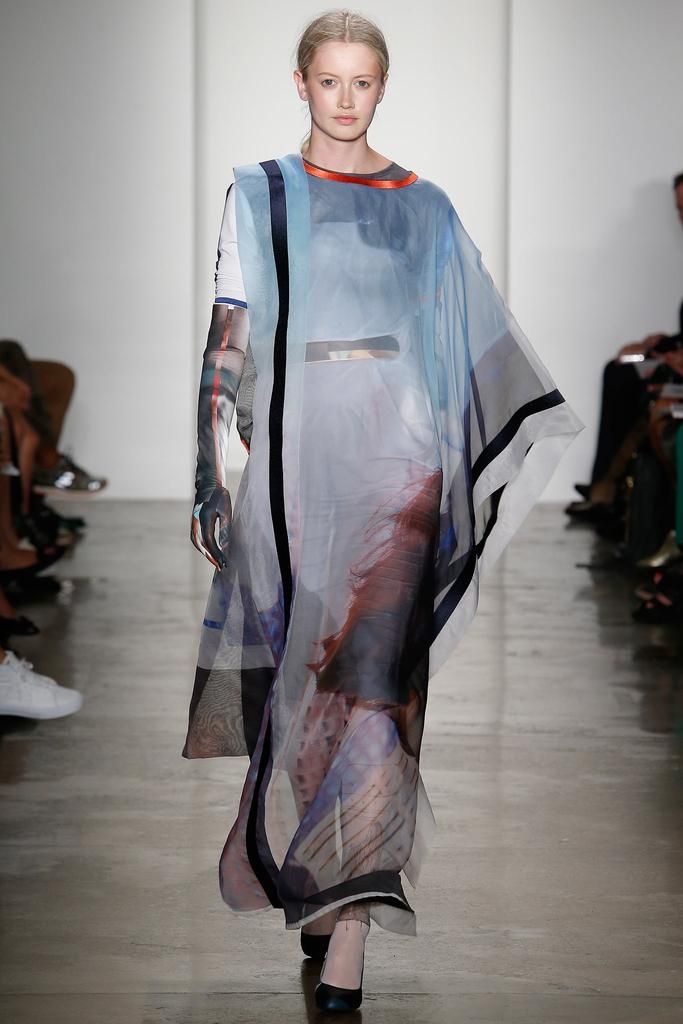 a fairskinned, blonde woman walks the runway in a fashion show. she is wearing a long, flowing dress made of chiffonlike material. the dress features a watercolor print in shades of blue, white, and reddishbrown. it is trimmed with black along the edges and has an orange accent at the neckline. the woman is wearing black heels and the photo captures a fulllength view of her as she confidently strides forward.