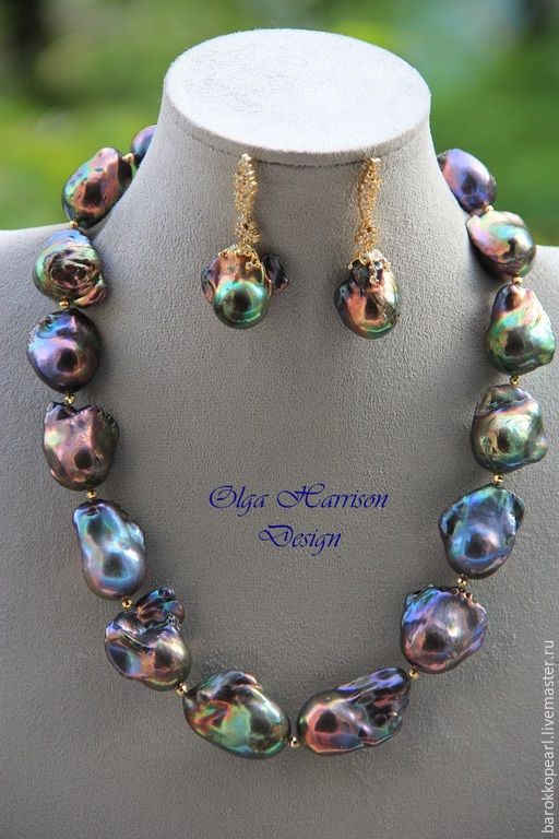 the image showcases a stunning jewelry set comprising a necklace and matching earrings. the necklace features large, iridescent baroque pearls in a rich spectrum of colors, ranging from deep greens and blues to shimmering purples and pinks.  the pearls have a unique, irregular shape, adding to their organic beauty. the earrings mirror the design of the necklace, each featuring a single baroque pearl suspended from a gold setting. the jewelry is displayed on a black bust, highlighting the vibrant colors of the pearls.
