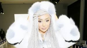 the image is a closeup portrait of a young woman wearing a luxurious, white furhooded coat. she has long, silver or light gray box braids that cascade down her shoulders.  her makeup is subtle yet elegant. the setting appears to be a fashion show or some kind of stylish event. the overall impression is one of high fashion and glamour.