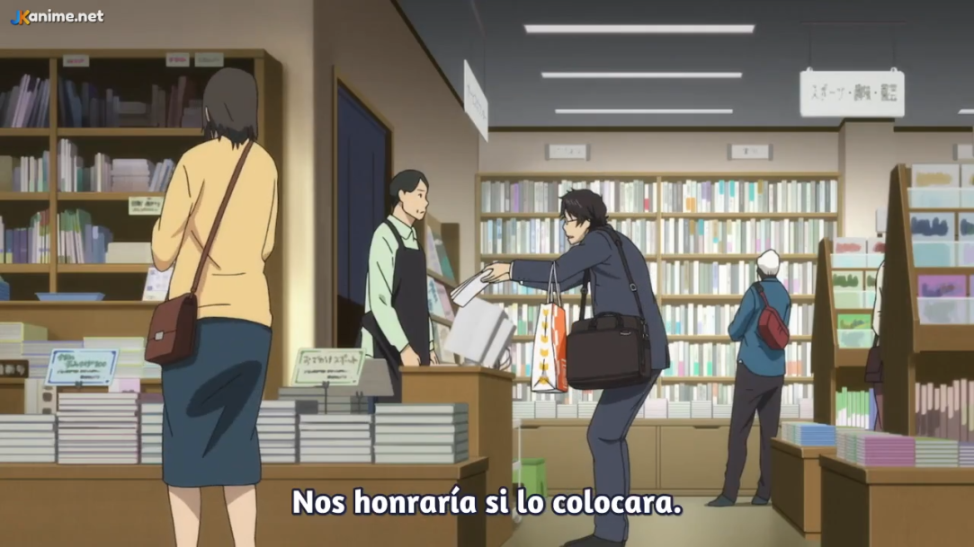 a man in a suit is handing a book to a cashier in a bookstore. the cashier is wearing a black apron and is standing behind a counter. a woman in a yellow shirt is standing to the left of the man in the suit. there are shelves of books in the background. the scene is lit by fluorescent lights.