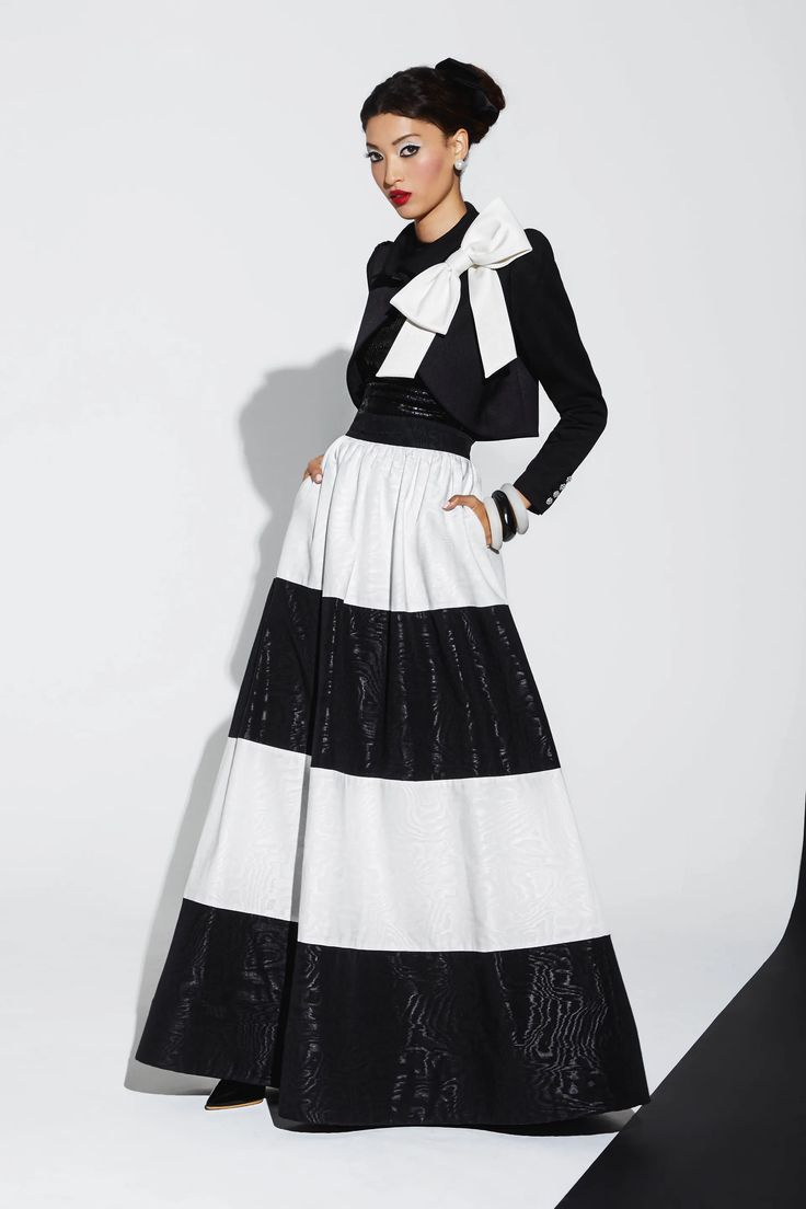 a woman in a black and white striped skirt with a large white bow on her black jacket is posing in a studio.