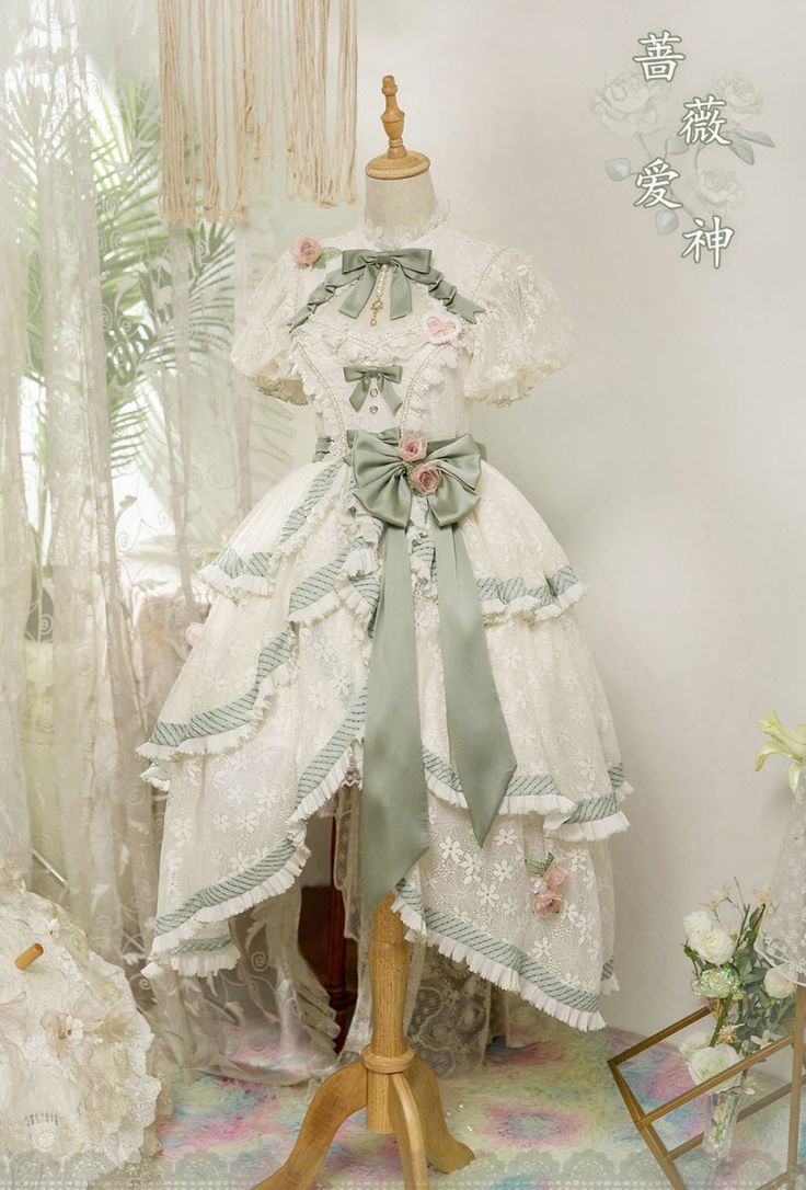 a white and green lolita fashion dress on a mannequin. the dress is adorned with lace, ruffles, bows, and floral details. the dress has a highlow hemline and a tiered skirt.