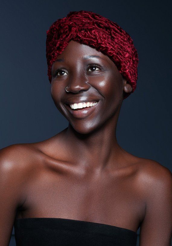 a closeup portrait of a black woman with a red head scarf smiling and looking away. she is wearing a strapless black top. the image is taken in a studio with a dark background.