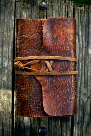this image shows a brown leatherbound journal, secured shut by a leather strap and buckle. the background consists of weathered wooden planks.