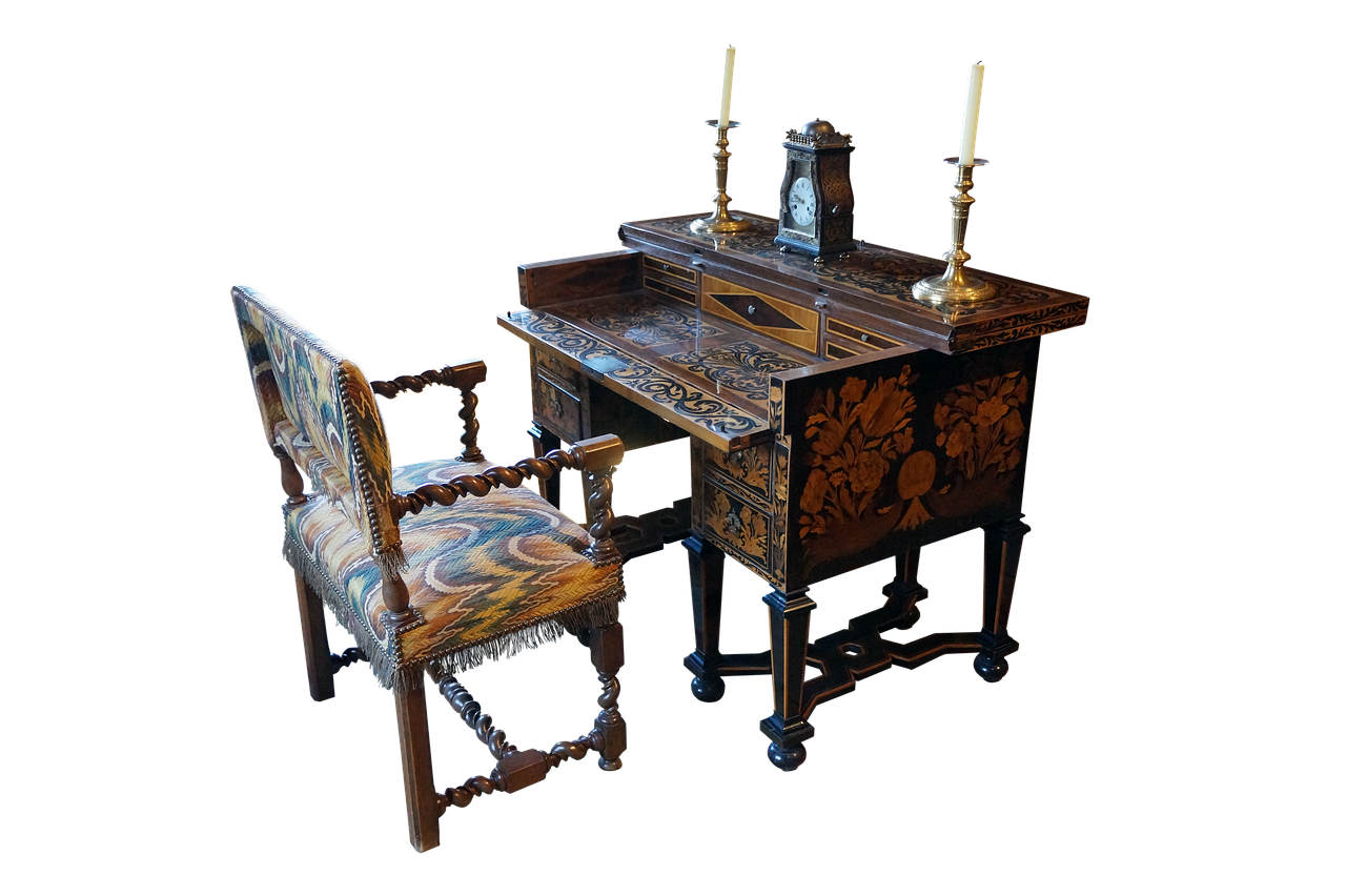 the image shows an antique writing desk and chair set against a black background. the desk is made of dark wood with elaborate inlaid patterns, including floral motifs. on top of the desk are two brass candlesticks with lit candles and a small clock. the chair is upholstered with patterned tapestry fabric and has a fringe trim. the chair and desk both feature ornate turned legs and a baroque style.