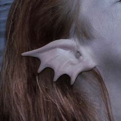 closeup of a person with long, red hair wearing a prosthetic elf ear. the ear is made of a pale, fleshtoned material and has a pointed, slightly curved shape. the ear is attached to the person's ear with adhesive.