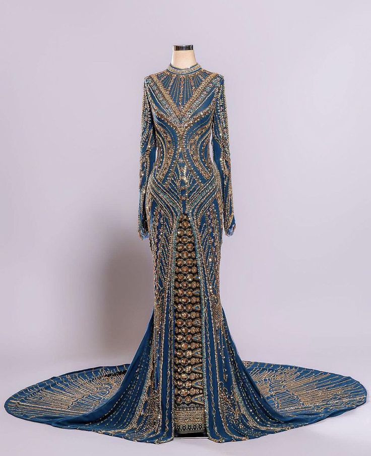 a long blue beaded formal dress with a mermaid shape. it features a long train and a high neckline. the dress has a high level of detail with gold beading and sequins. the dress is perfect for a special occasion like a wedding or prom.