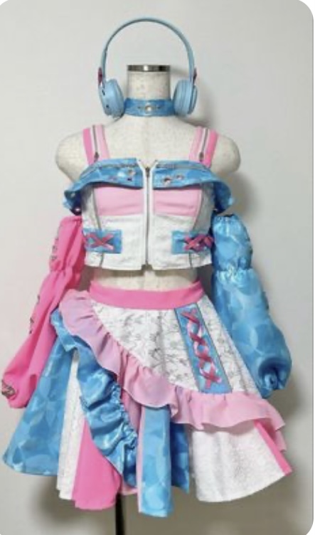 a colorful, frilly outfit with a cropped jacket, short skirt, and detached sleeves displayed on a mannequin. the outfit is primarily pink, blue, and white with silver accents. the mannequin is wearing blue headphones and a black choker.