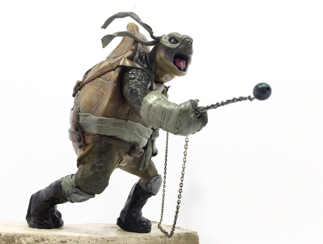 a sculpture of a teenage mutant ninja turtle is shown. the turtle is wearing a shell and a headband. he is holding a mace in his hand. the sculpture is on a pedestal.