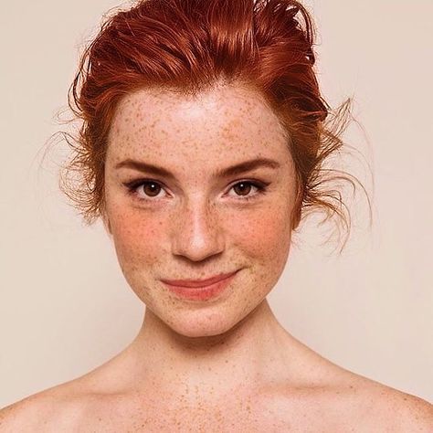 a close up portrait of a woman with long red hair smiling at the camera. she has freckles and rosy cheeks.