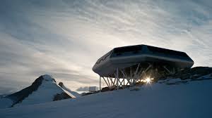 a futuristic building stands on a snowy mountain top against a backdrop of clouds. the building is made of sleek, white lines and appears to be modern and abstract. the surrounding area is covered in snow, creating a cold, wintery scene.