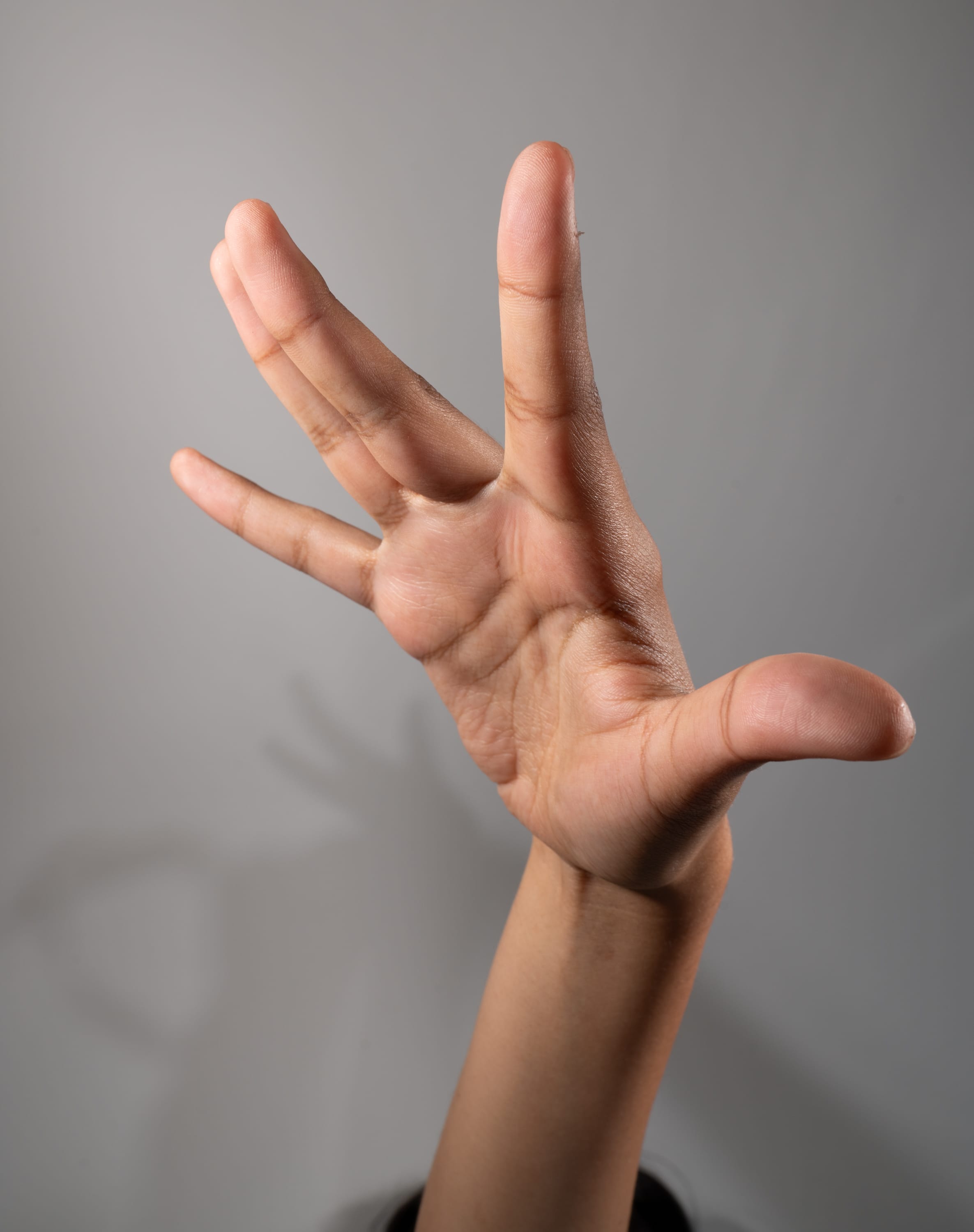 the image shows a hand with its fingers spread apart, held up against a gray background. the hand is positioned in a way that suggests a gesture or sign. the lighting is soft, creating subtle shadows that enhance the contours of the hand.
