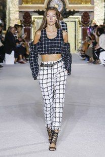 a fashion model walks the runway in a stylish outfit. she is wearing a black and white plaid cropped top and matching high waisted pants.  she has a belt around her waist. the model is posing for the camera, looking stylish and confident.