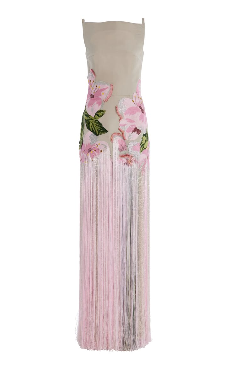 a sleeveless evening gown made from beige fabric is adorned with pink floral patterns and features a pink fringe detail.