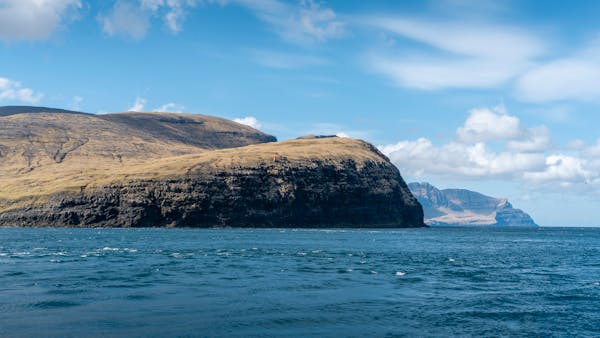 the image captures a breathtaking vista of a rugged coastline under a vibrant sky. imposing cliffs, cloaked in shades of green and brown, rise dramatically from the deep blue sea. the azure sky is dotted with fluffy white clouds, casting playful shadows on the water's surface. the composition evokes a sense of tranquility and the raw beauty of nature.