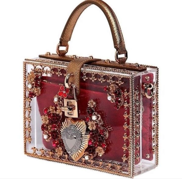 a box clutch purse with a clear acrylic exterior showcasing red fabric inside, decorated with gold embellishments, floral accents, and a heartshaped emblem. it features a top handle, a padlock, and decorative hardware.