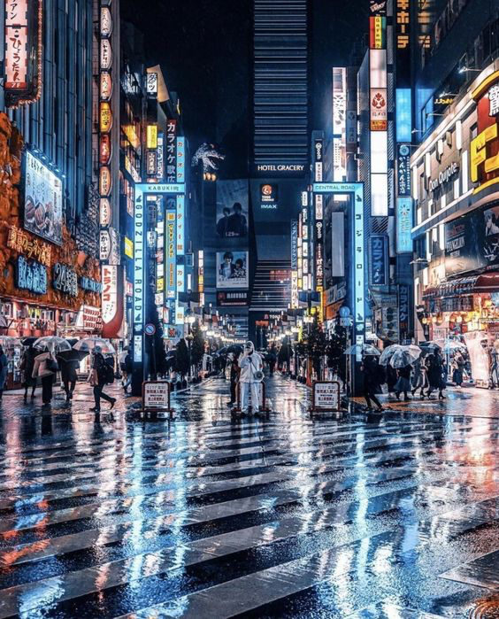 a bustling street in japan, likely tokyo, at night. the street is crowded with people walking, with bright neon signs illuminating the buildings. the ground is wet, reflecting the lights, giving the scene a vibrant and dynamic feel.