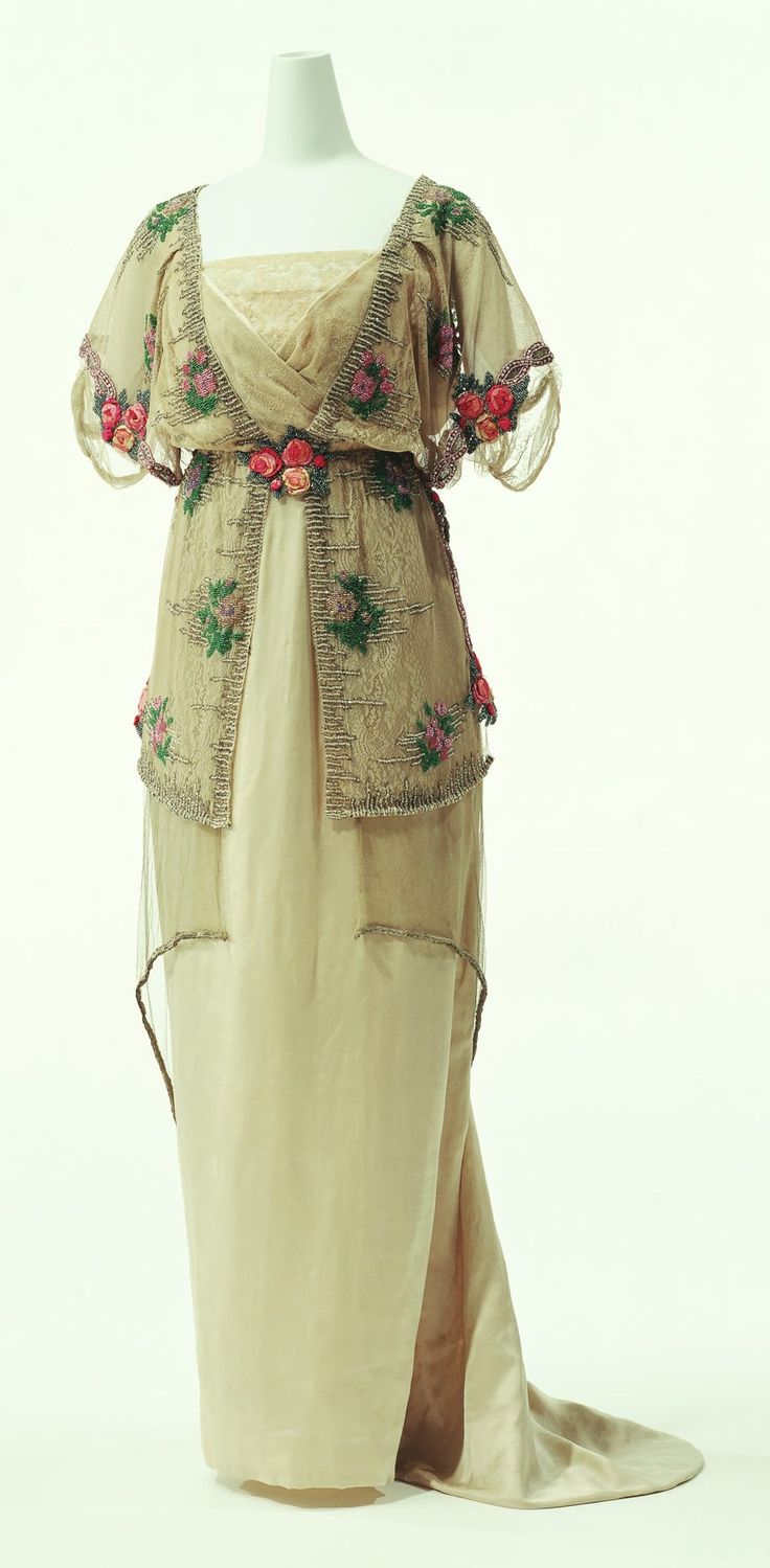 a vintage edwardian evening gown with a sheer lace overlay, beautifully embroidered with silk flowers, showcasing a delicate and feminine design. the gown features a graceful, flowing silhouette with a long train, highlighting the elegance of the era. the gown's intricate details and sumptuous fabrics reflect the opulence of the belle epoque, making it a timeless and exquisite example of early 20thcentury fashion.