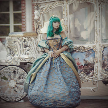 the image shows a woman with vibrant green hair, wearing a stunning, elaborate blue and gold ball gown. she is positioned next to an antique, white horsedrawn carriage, richly detailed with ornate carvings and painted panels. the overall aesthetic is fairytalelike, suggesting a princess or fantasy character. the setting, the woman's attire, and the carriage create a scene evocative of a bygone era, possibly inspired by historical or baroque/rococo styles. the photo appears to be a professional photoshoot, capturing the details of the costume and the setting with artistic lighting and composition.