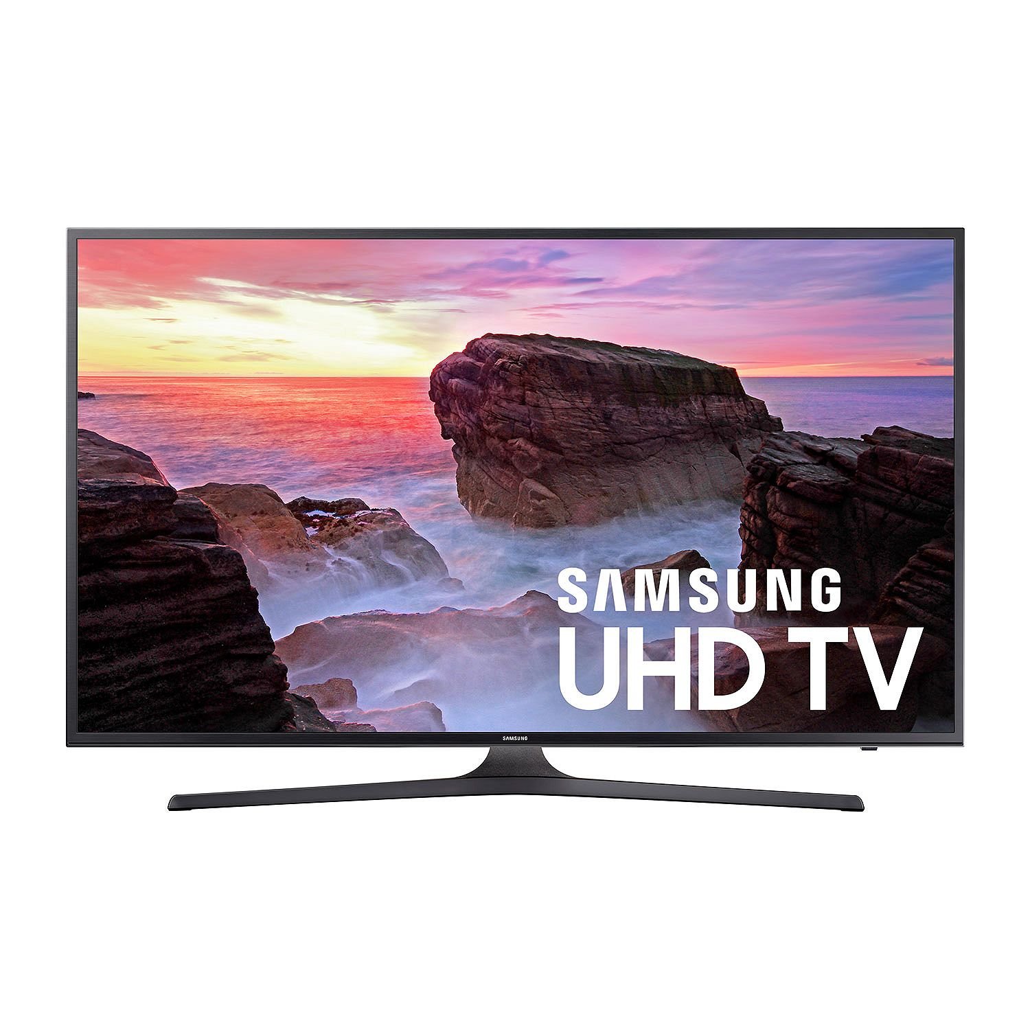 the image shows a samsung uhd tv displaying a scenic view of a rocky coastline at sunset. the tv is standing on its stand and the screen shows waves crashing against rocks under a colorful sky. the "samsung uhd tv" logo is prominently displayed on the screen.
