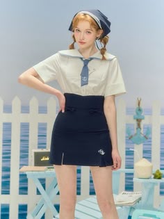 a young woman is wearing a sailor uniform with a white shirt and blue skirt and a blue hat. she is standing outside and smiling for the camera. she is wearing a cute and stylish outfit.