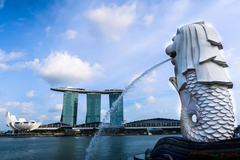 a closeup shot of the merlion statue in singapore, with the iconic marina bay sands hotel in the background. the statue is spewing water from its mouth, creating a dramatic fountain effect. the sky is blue with white clouds, and the water is calm and reflecting the surrounding scenery. this image is a popular tourist destination and a symbol of singapore.