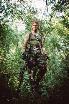 a man dressed in camouflage clothing and tactical gear stands in a lush green jungle. he is armed with a rifle and has a determined look on his face.  the dense foliage surrounds him, creating a sense of concealment and immersion in the natural environment. the overall impression is one of military action or survival in a wilderness setting.