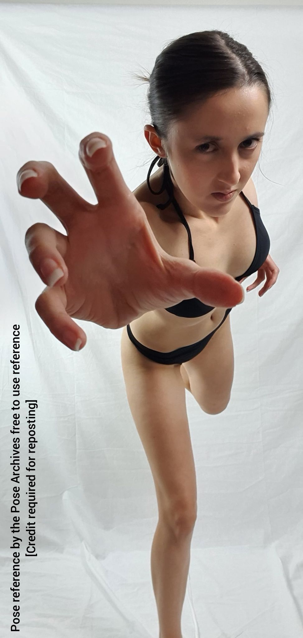 a woman in a black bikini is captured in a dynamic pose against a white backdrop. shot from a low angle, she extends her hand towards the viewer, creating a sense of movement and engagement.```