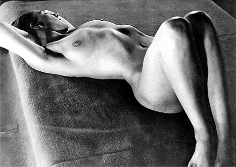a black and white photograph of a nude female reclining on a textured surface.  the woman is positioned with her arms extended behind her and her legs bent. the image emphasizes the form and curves of the body, with strong contrasts in light and shadow. the texture of the surface she lies on is clearly visible. the overall style is classic and artistic.