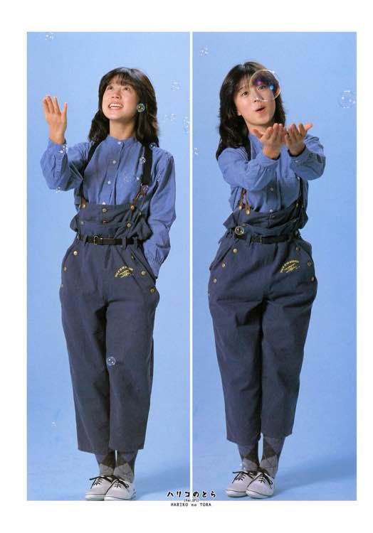 a young japanese woman in a blue buttonup shirt and dark blue overalls is posed in two different positions against a light blue background. she is smiling and has long brown hair, with white sneakers on her feet. there are small bubbles in the air. the text at the bottom of the image reads "haruko no tora."