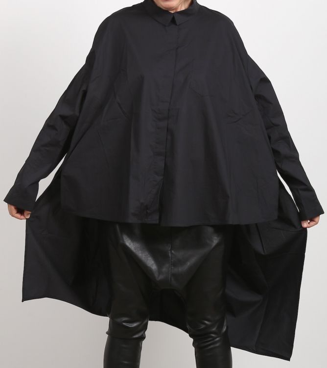 a person wearing a black, oversized shirt and baggy leather pants stands against a white background. the shirt is longsleeved and buttoned, extending down past the hips, and the pants appear to be made of shiny black leather. the outfit gives a modern, stylish look.