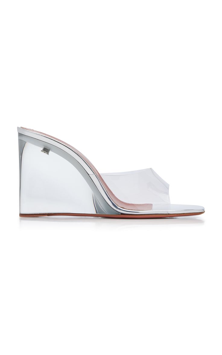 the image shows a pair of women's transparent wedge sandals.  the shoes are clear pvc with a silvertoned wedge heel. they are opentoed mules, meaning they slip on and have no straps. the heel is a substantial wedge, and the insole appears to be a light brown or nude color. the shoes are presented on a white background, emphasizing their sleek and modern design.