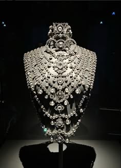 a closeup shot of a diamond necklace worn by a mannequin. the diamond necklace is elaborate and shiny, with various sized diamonds. the necklace is very expensive and rare.  the mannequin is wearing a black dress, so the necklace is the focal point of the image. the necklace is on display in a welllit room.  the image is taken from an angle, showcasing the beauty of the necklace.