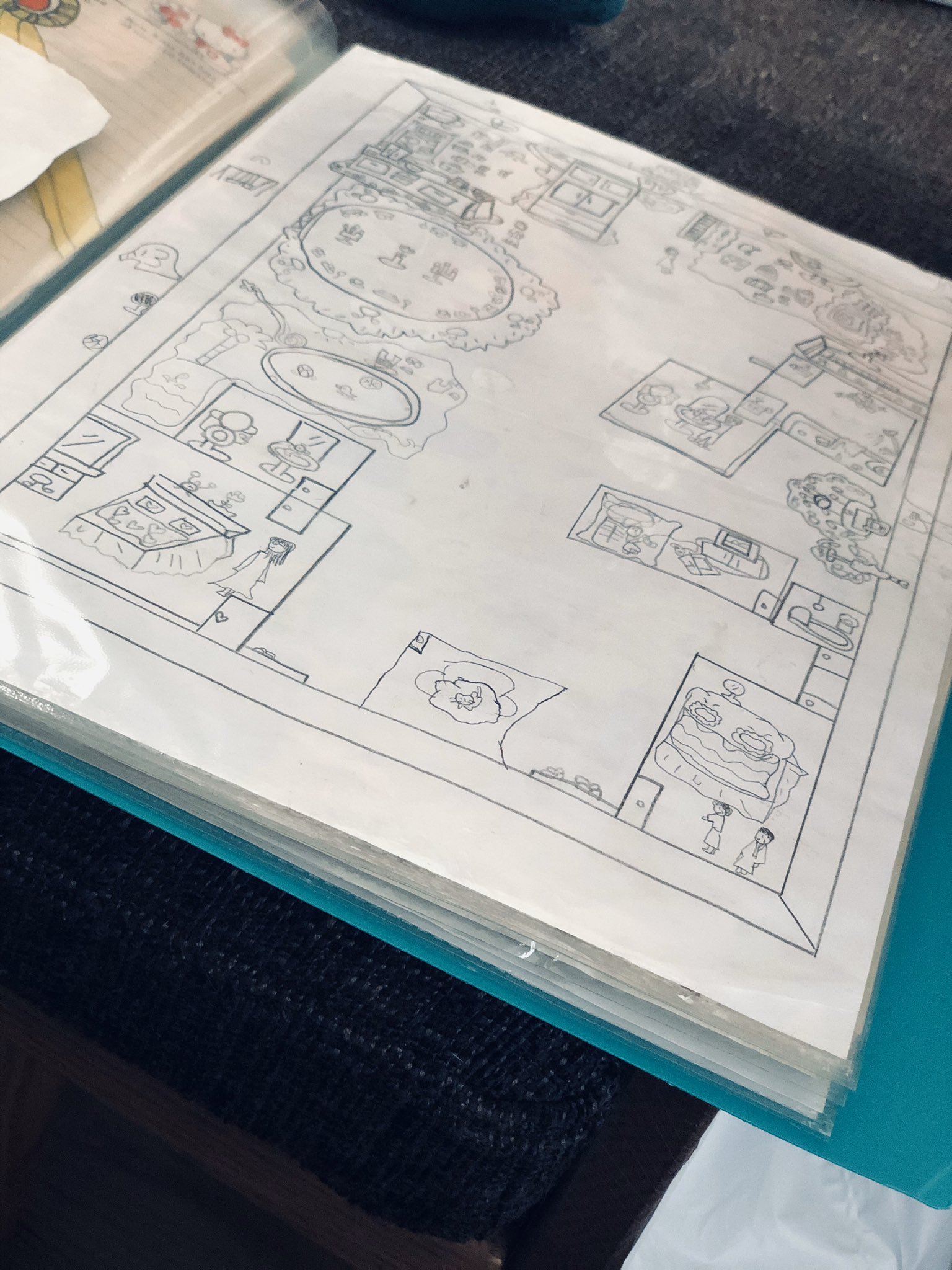 a child's handdrawn floor plan of a house, showing different rooms and furniture. it is drawn in black marker on white paper and is displayed in a clear plastic sheet protector.  the drawing style is simple and imaginative.