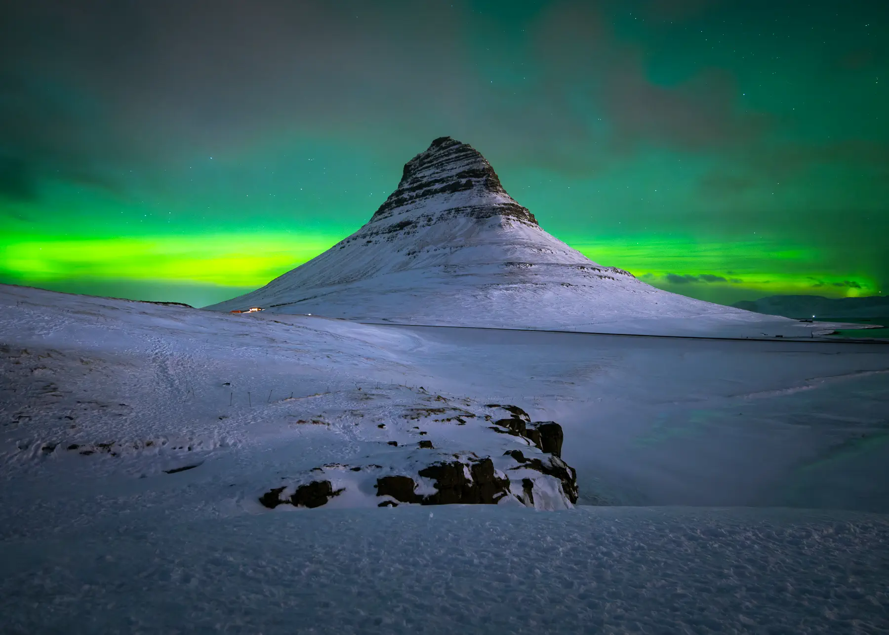 a majestic mountain, covered in snow, stands tall against a vibrant green sky, illuminated by the mesmerizing aurora borealis. the northern lights dance across the horizon, casting a magical glow on the winter landscape.  stars twinkle above, adding to the celestial spectacle. this aweinspiring scene captures the raw beauty and wonder of iceland's natural wonders.
