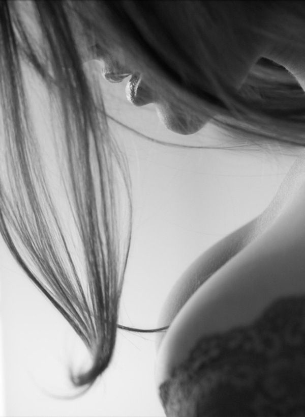 the image is a closeup, black and white portrait of a woman.  her face is partially obscured by her long, flowing hair which cascades down her body. only part of her face, including her lips and part of her jawline, is visible. her upper body is also shown, revealing a glimpse of her shoulder and breast, partially covered by what appears to be lacy lingerie. the overall mood is sensual and intimate, with soft lighting and a focus on the woman's curves and delicate features. the style is artistic and evocative, leaving some elements to the viewer's interpretation.