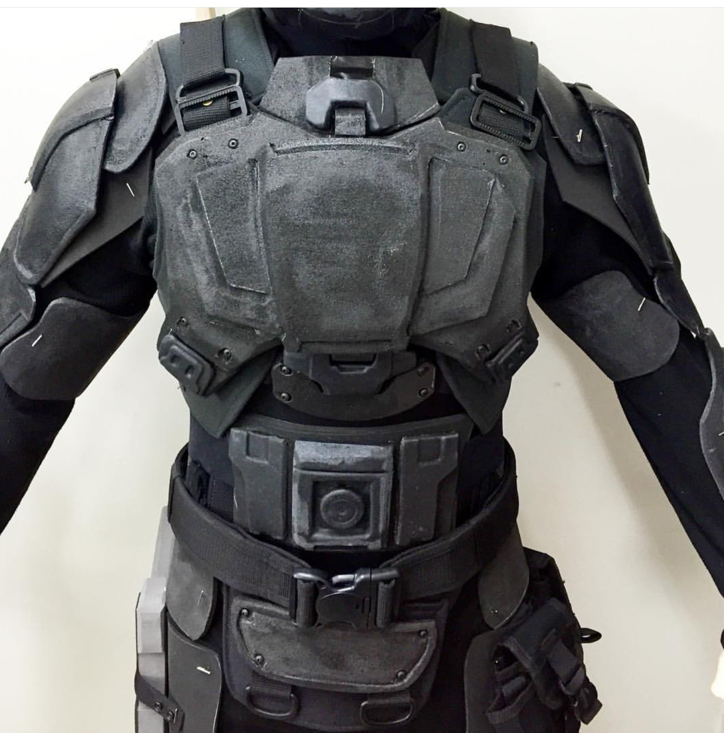 close up of a person wearing black futuristic body armor. the armor has intricate details and is made of a hard, durable material. the chest plate is prominent and includes a small window or display. the person is wearing a black suit underneath the armor, and they are holding a black weapon. the background is white, and the overall image is dark and gritty. the armor appears to be wellmade and functional, suggesting its use in combat or other dangerous situations. the overall image is evocative of scifi and futuristic action.