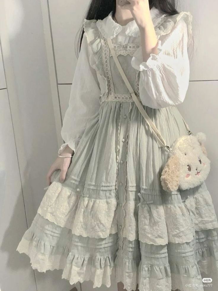 a young woman is taking a mirror selfie, showcasing her elegant lolitainspired outfit. she's wearing a flowy, light green dress with intricate lace details, layered over a white blouse with delicate lace accents. her outfit exudes a soft and feminine aesthetic. the background reveals a glimpse of a clean and welllit interior, hinting at a tidy and organized space.