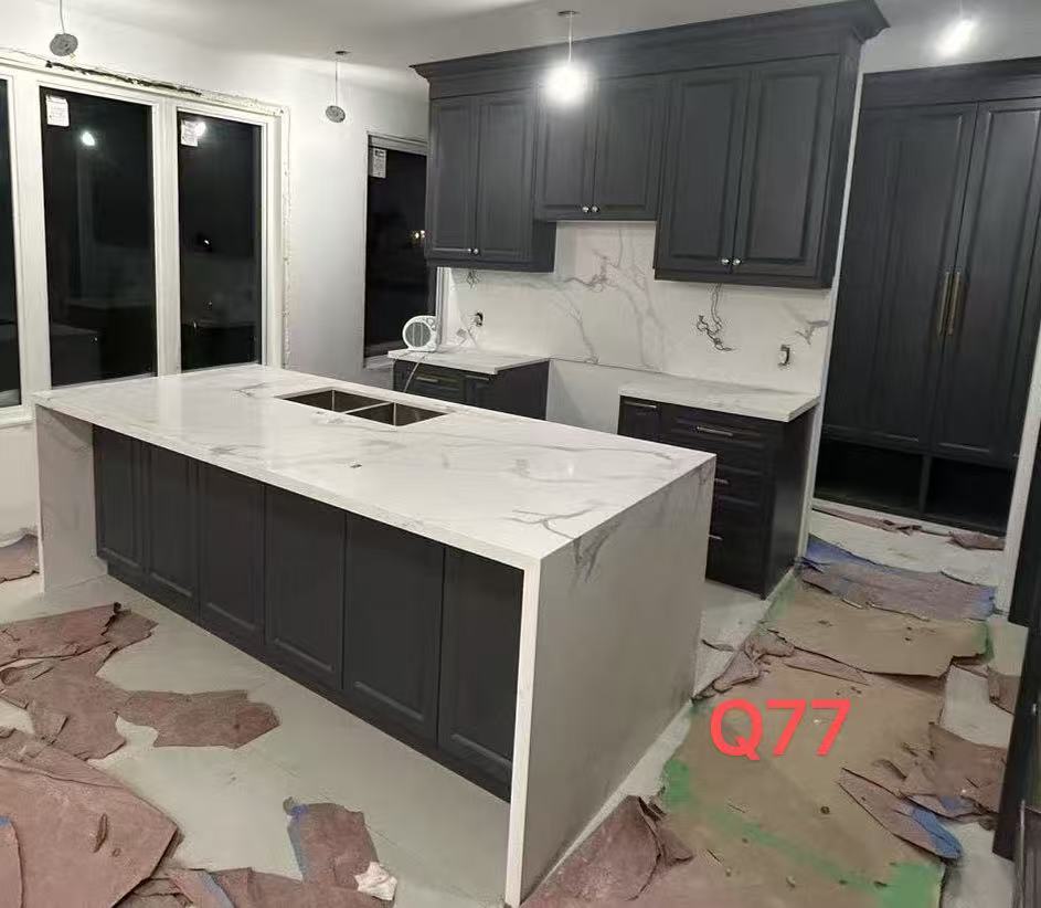 a kitchen under construction with dark cabinets, a marble countertop island with a sink, marble backsplash, and flooring being installed.