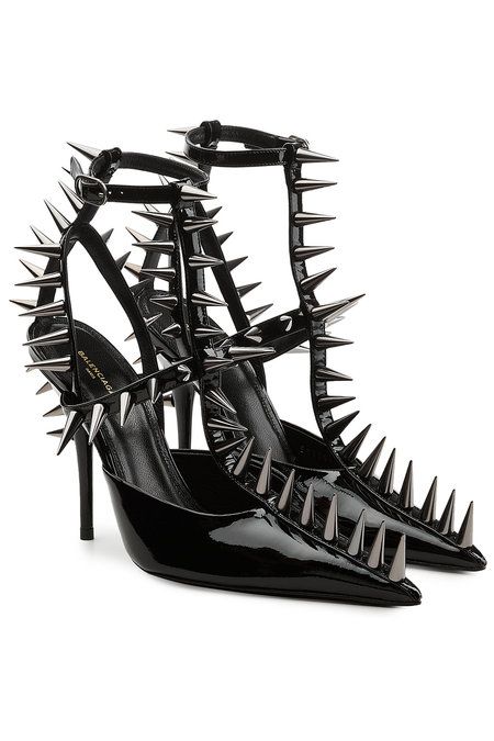 a pair of black patent leather balenciaga spiked heels are shown. the shoes are tstrap style with metal spikes covering the straps and extending onto the heels.  the shoes are positioned with one shoe slightly in front of the other, showcasing the detail of the spikes and the sleek design.  the background is plain white, focusing attention on the shoes.
