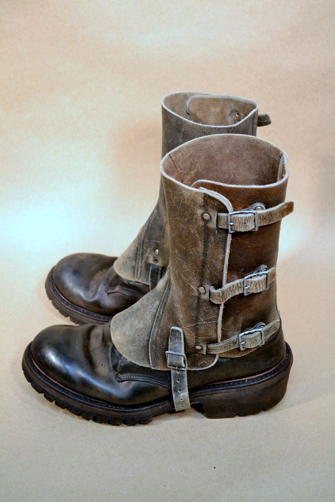 this is a close up image of a pair of brown leather boots with buckles and straps. the boots are vintage and look well worn. they are made of a thick leather and have a sturdy sole. the boots are laced up and have a buckle on the side. the boots are sitting on a light brown background.