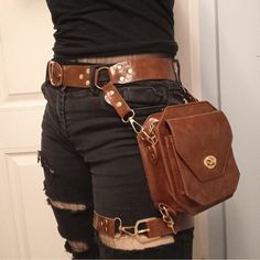 a person is wearing a brown leather hip bag with gold hardware. the bag is attached to a belt and has adjustable straps. the person is also wearing black pants.