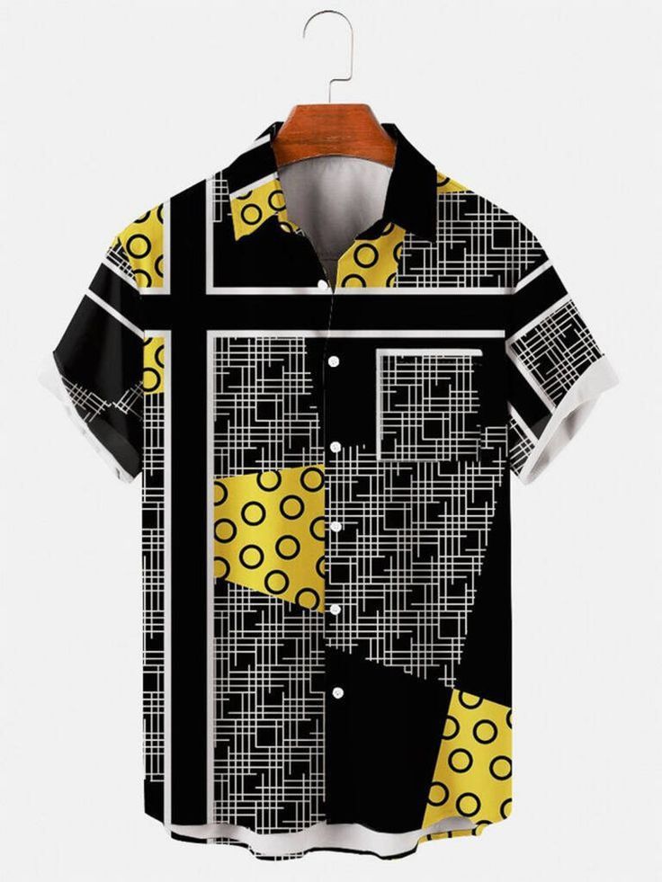 a shortsleeved buttondown shirt with a geometric pattern of black, yellow, and white squares and circles hangs on a wooden hanger against a light gray background.
