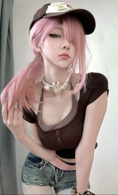 a young woman with pink hair and a brown cap is wearing a brown shirt and blue jean shorts. she is smiling and looking down.