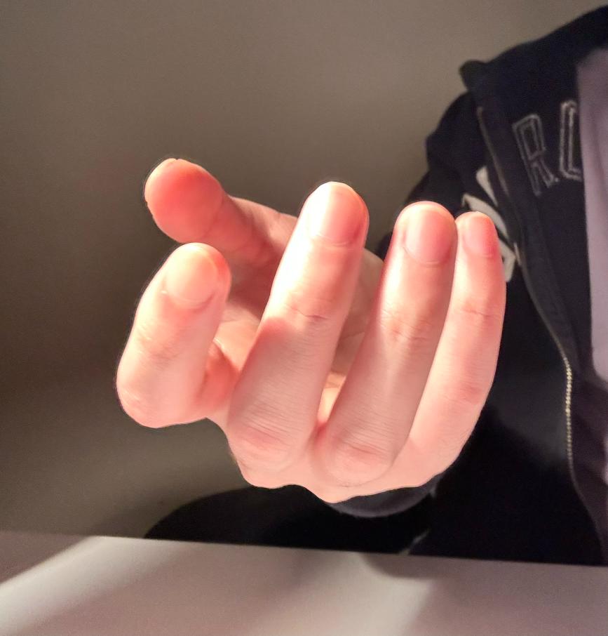 a closeup shot of a fairskinned hand reaching toward the viewer. the hand is illuminated by warm, indoor sunlight, creating visible shadows on the palm and fingers.  the person is wearing a black jacket with white lettering.