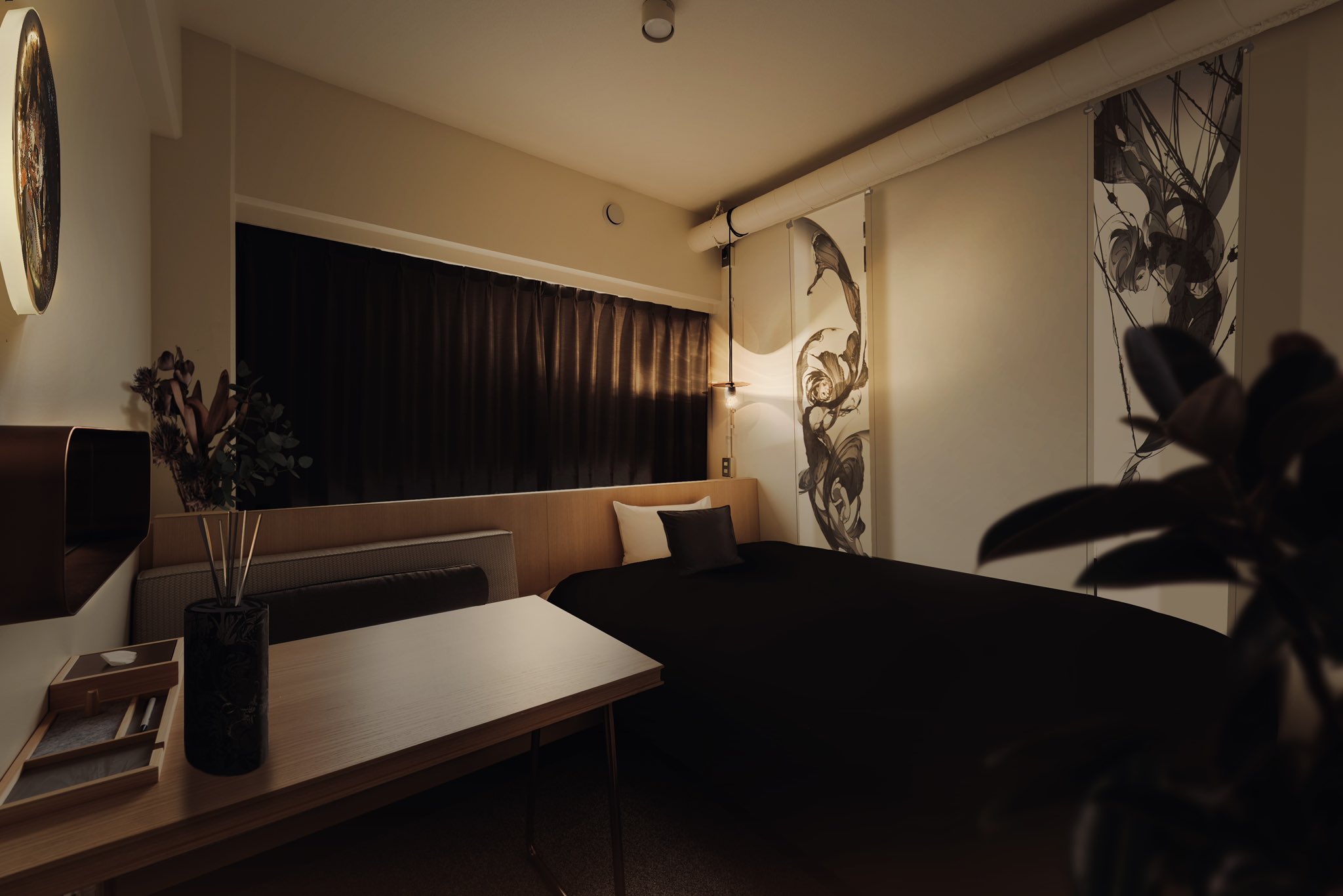 a dimly lit, modern bedroom with a double bed, desk, and artwork on the walls. the color scheme is muted and calming, with an emphasis on natural materials like wood and fabric. a plant in the corner adds a touch of life to the space.