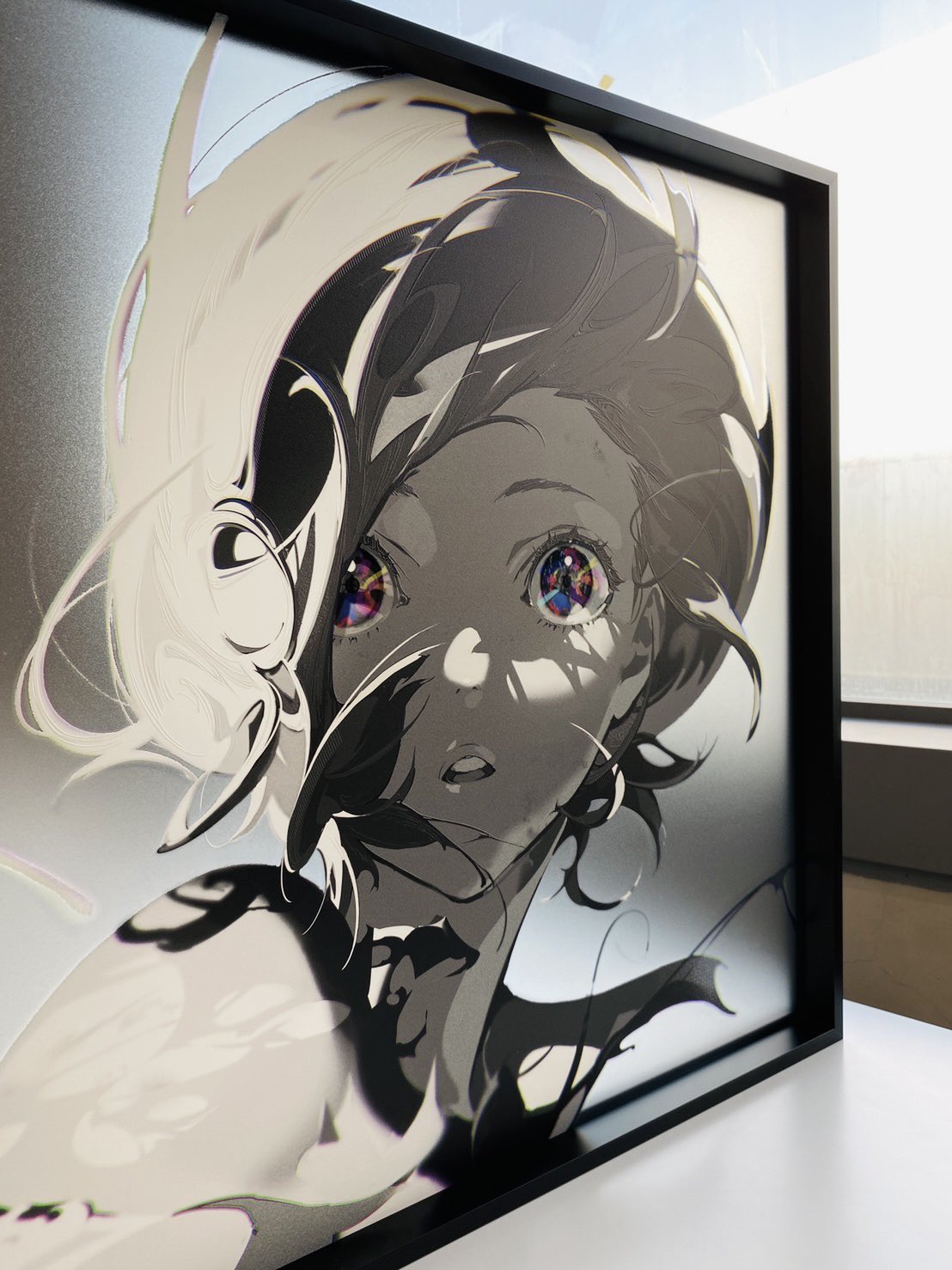 a framed print of a stylized anime girl with flowing hair and bright eyes hangs on a wall in an art gallery. the print is in grayscale with splashes of color in the girl's eyes, and the image is slightly obscured by reflections from the gallery's windows.