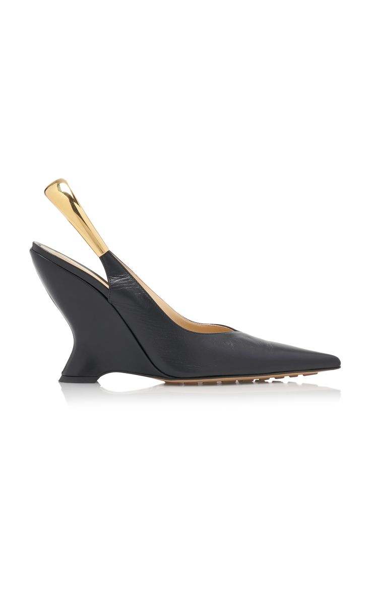 a pair of black leather slingback wedge heels with gold detailing on the slingback strap. the shoes have a pointed toe and a wedge heel. the shoes are isolated on a white background.